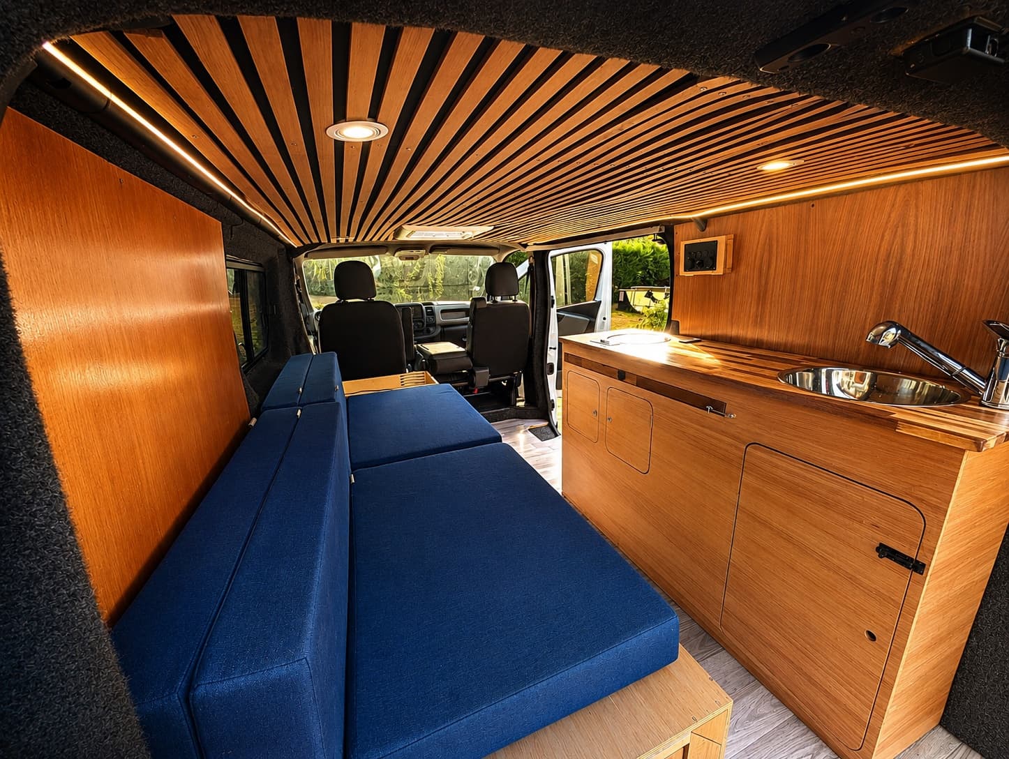 Intérieur d'un van aménagé Vanzon : banquettes, cuisine en bois et plafond en tasseaux